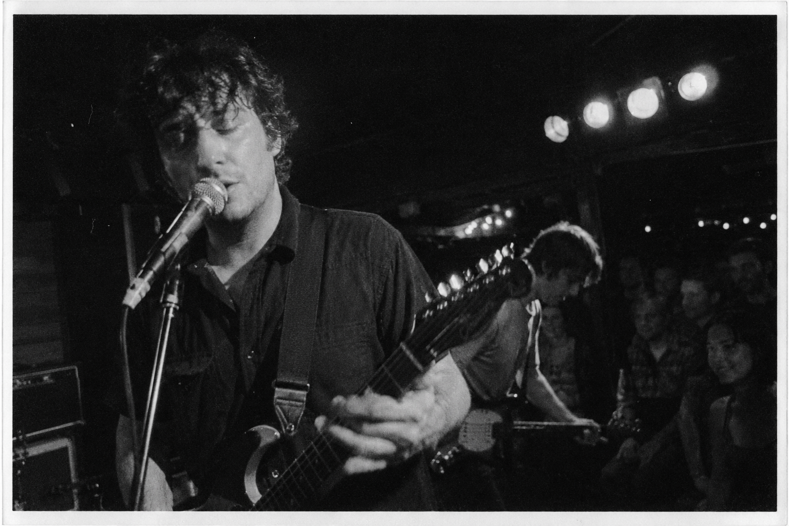 Grainy black-and-white photograph of musicians performing in a small dimly lit venue.